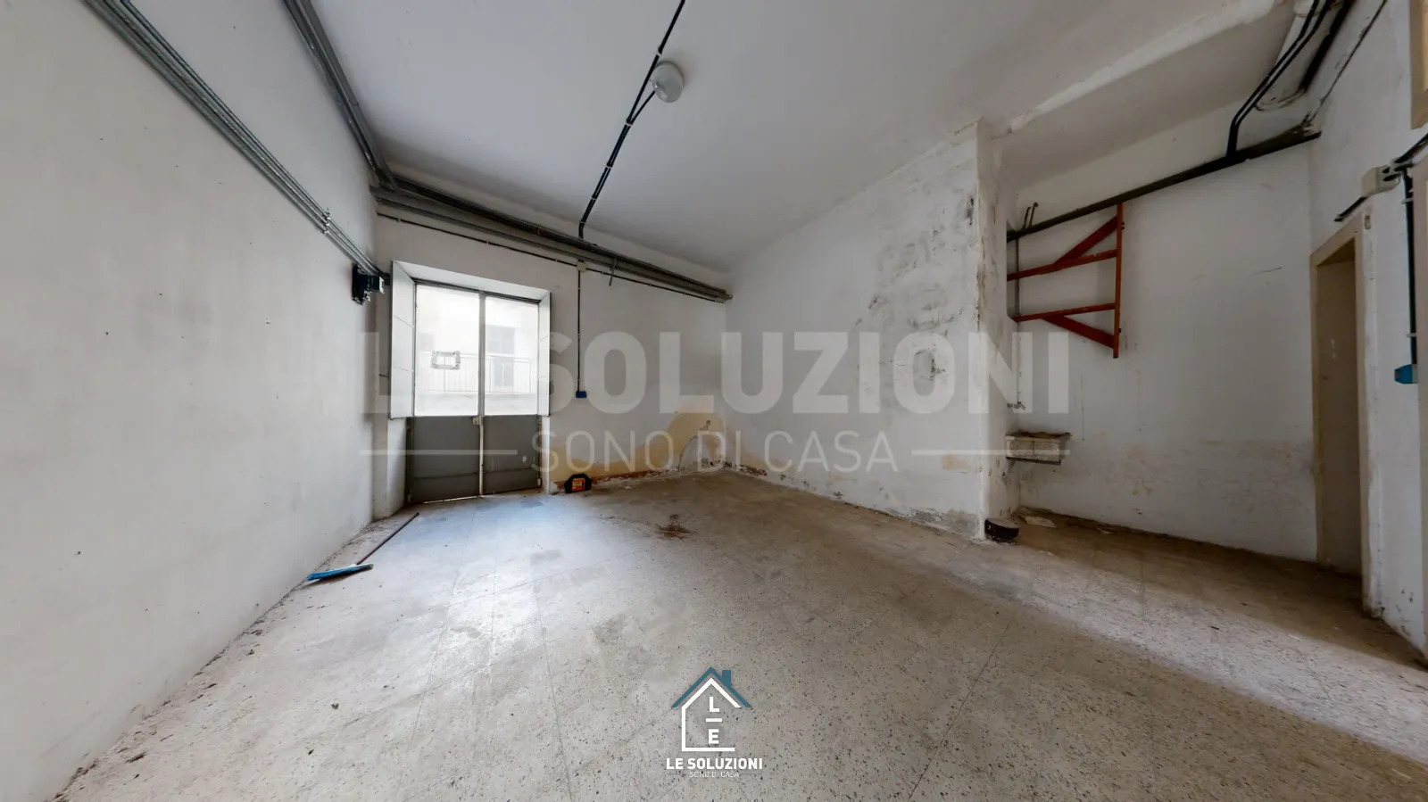 Locale grezzo con umidità alle pareti e finestra su cortile – Appartamento a Putignano